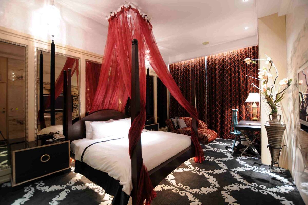 A four-poster bed with a canopy, a bedside table, a chair, and a potted plant.