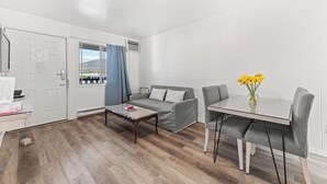 A modern, well-lit room with a sofa, a dining table with chairs, and a small coffee table. - 5000 Motel (Penticton)