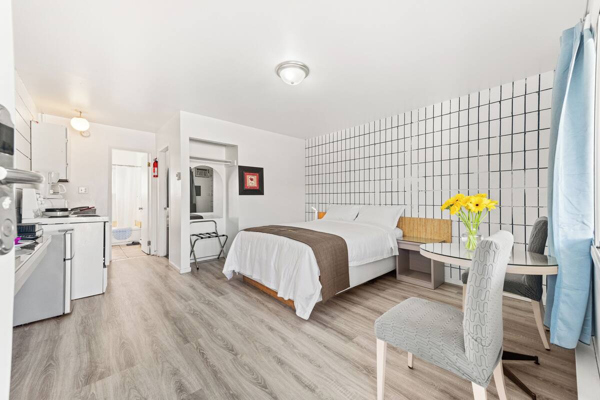 Una camera d'albergo moderna con un letto, una scrivania, una sedia e un piccolo angolo ristoro.
