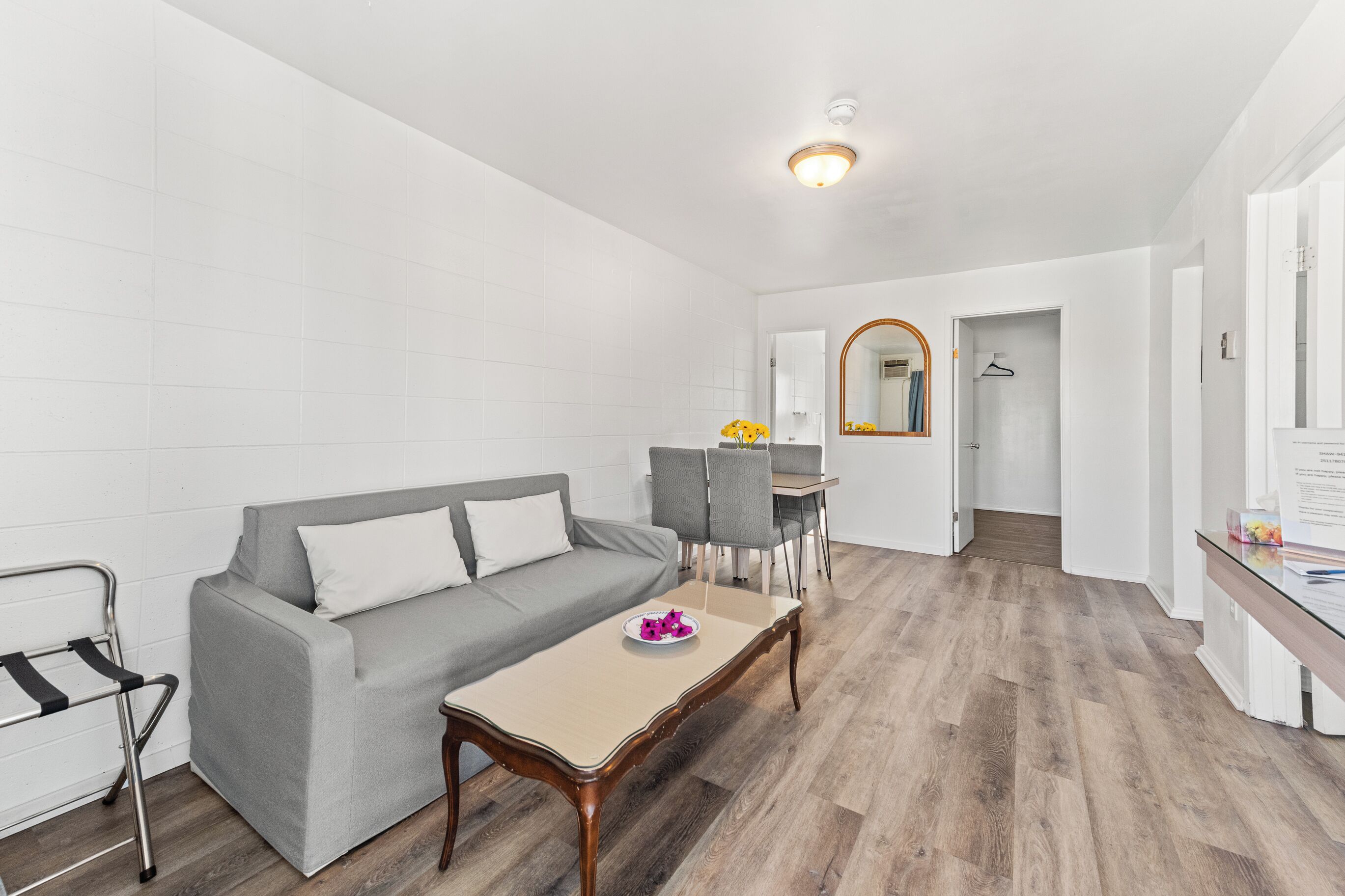 A modern living room with a grey sofa, a wooden coffee table, and a dining area with grey chairs.