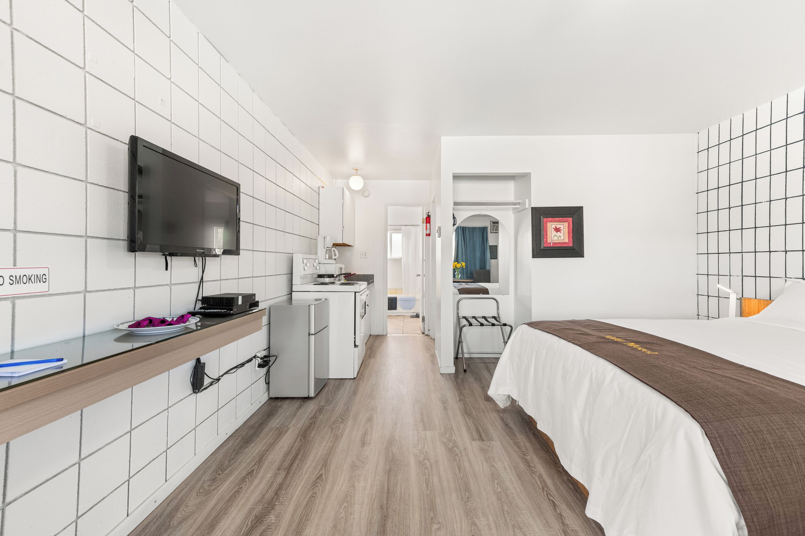 A compact hotel room with a kitchenette, a bed, a TV, and a bathroom visible through an open door.