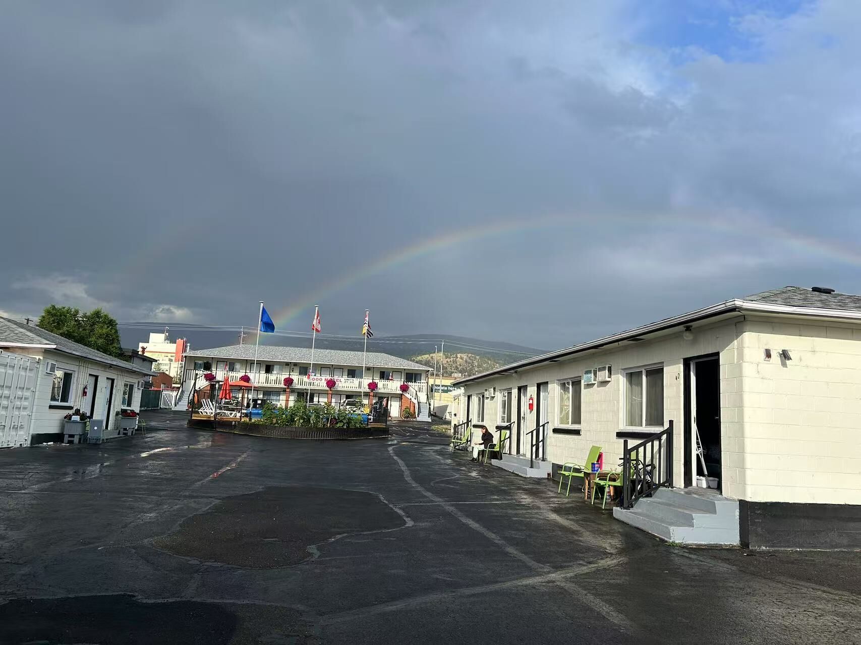 A motel with a central building and several smaller units, a parking lot, and a rainbow in the background.