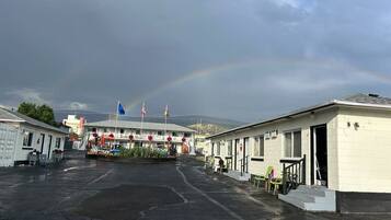 A motel with a central building and several smaller units, a parking lot, and a rainbow in the background.