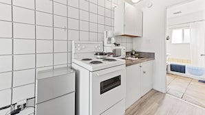 A compact kitchen with white cabinets, a stove, a microwave, and a sink. - 5000 Motel (Penticton)