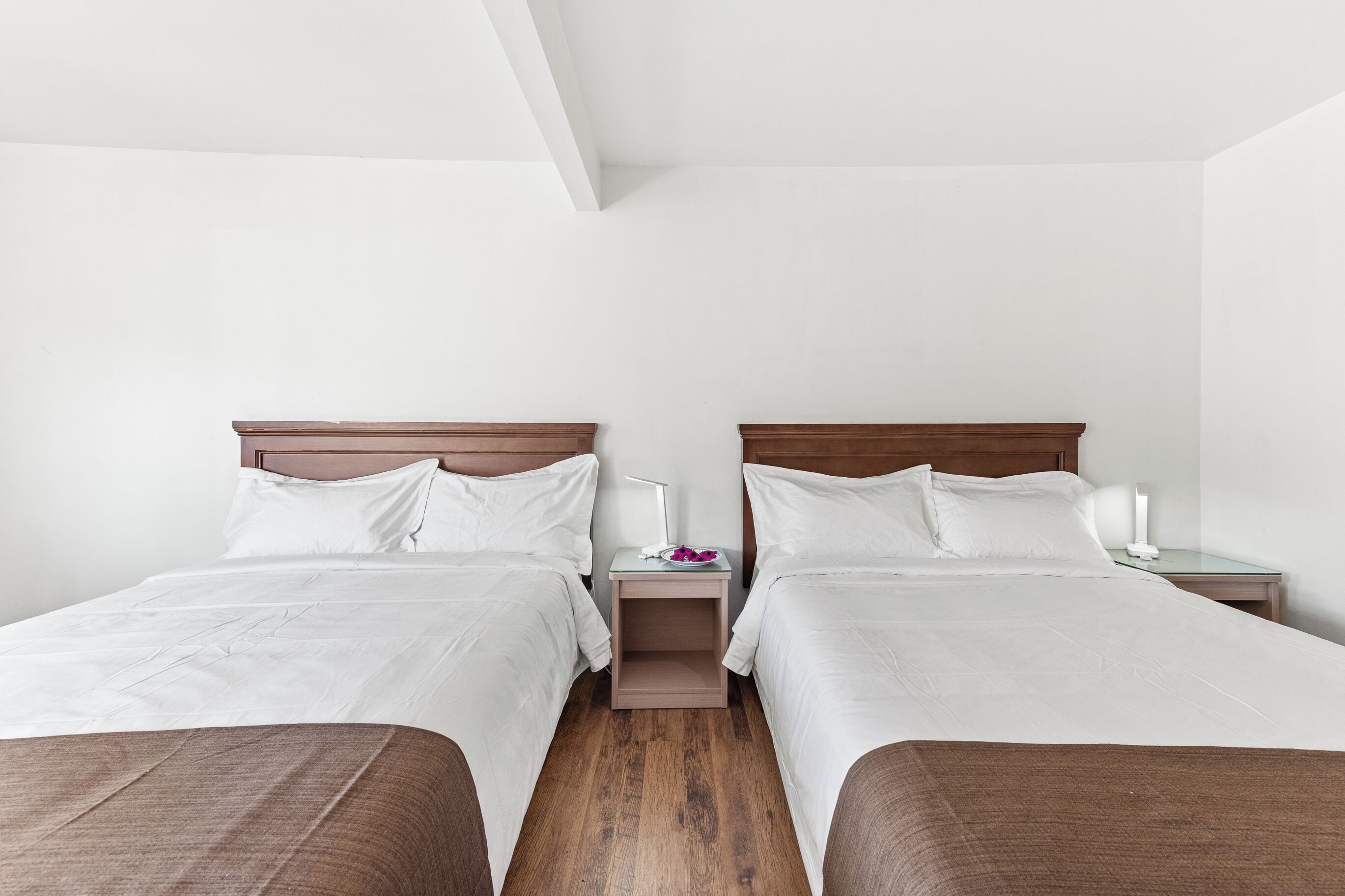Ein Hotelzimmer mit zwei Betten, einem Nachttisch mit Lampe und einem kleinen Tisch mit Blumenvase.