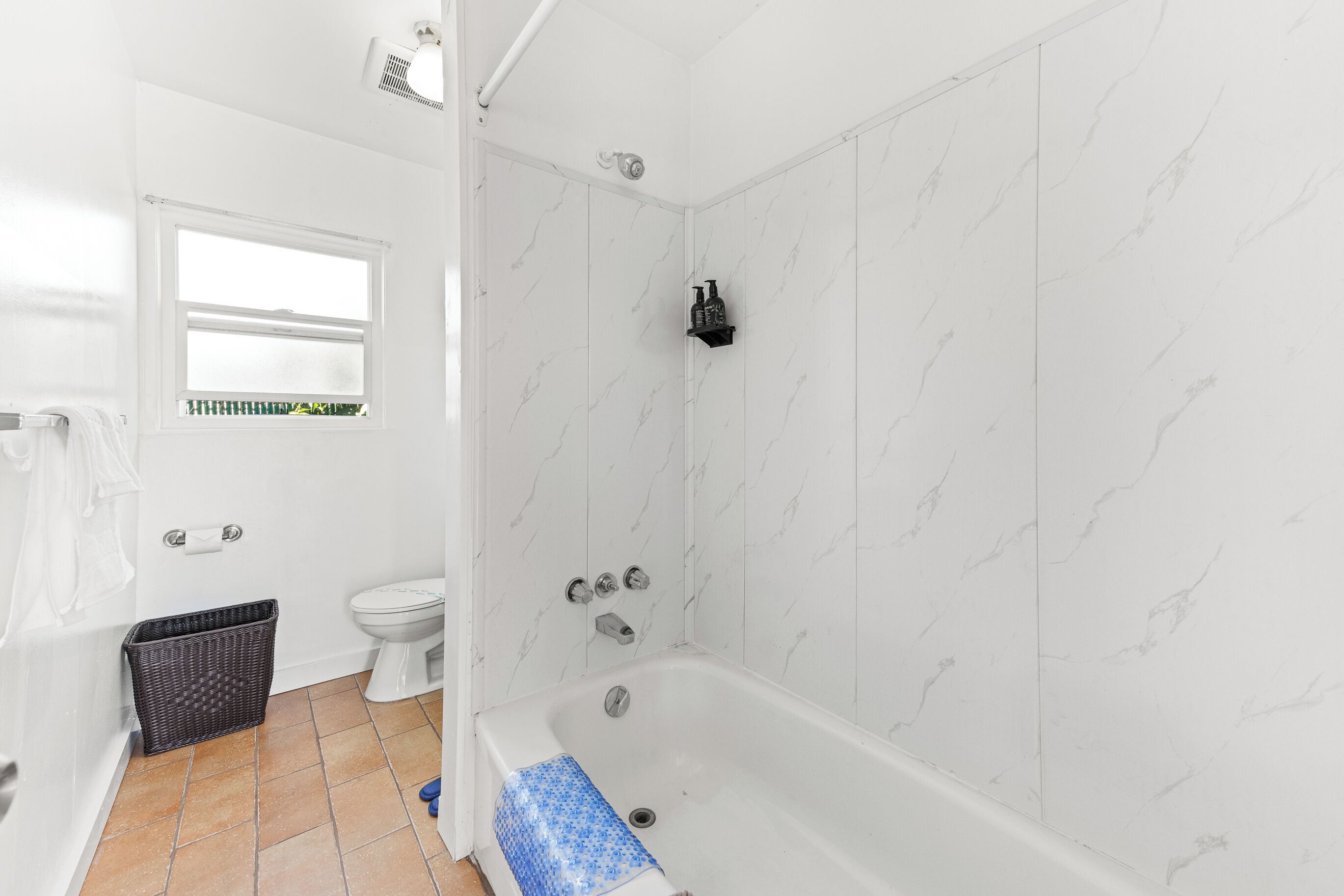 Un baño con pared de mármol blanco, una bañera blanca, un inodoro y un ventanal.