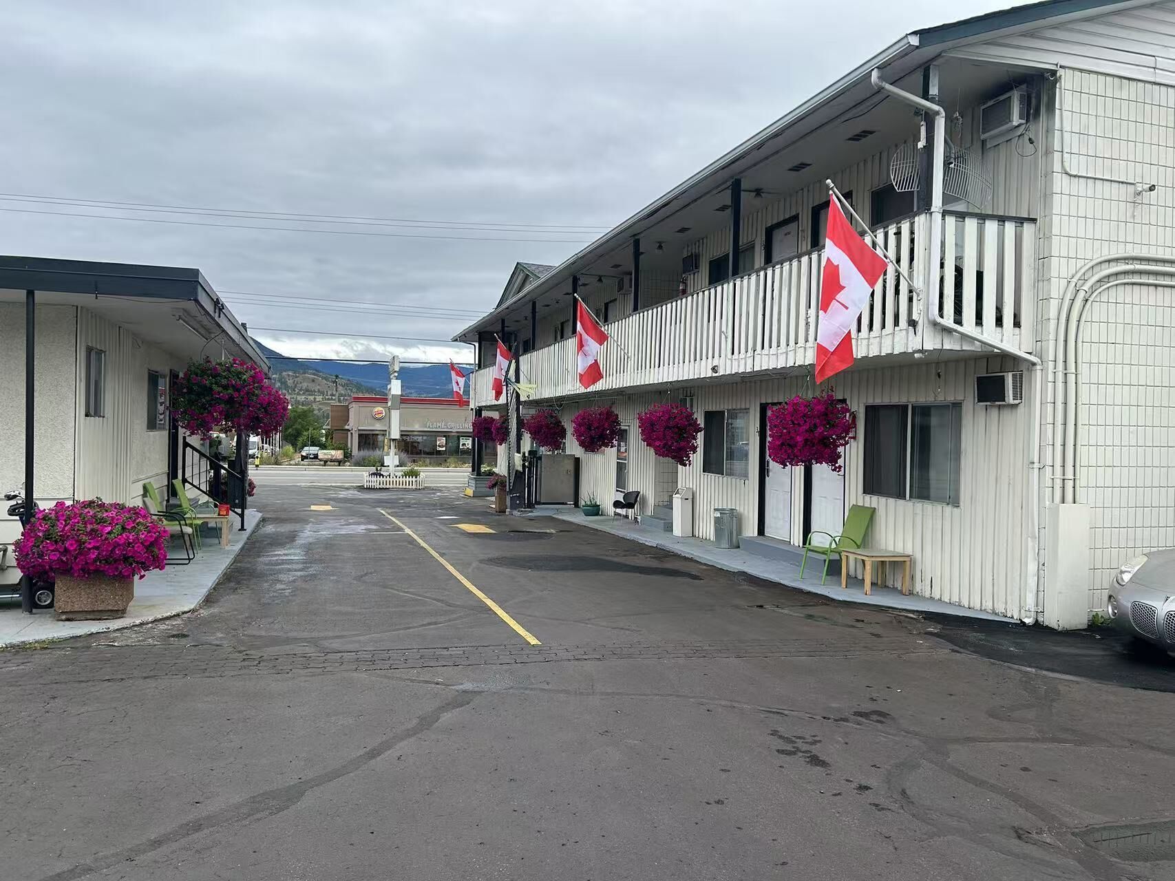 Fila de edificios de motel blancos con banderas rojas y blancas, cestas de flores rosadas y una carretera despejada al frente.