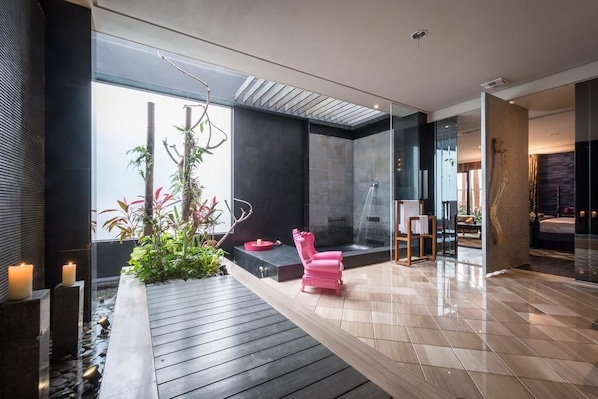 Un interior moderno con suelo de madera, una silla rosa, una planta pequeña y un separador de vidrio.