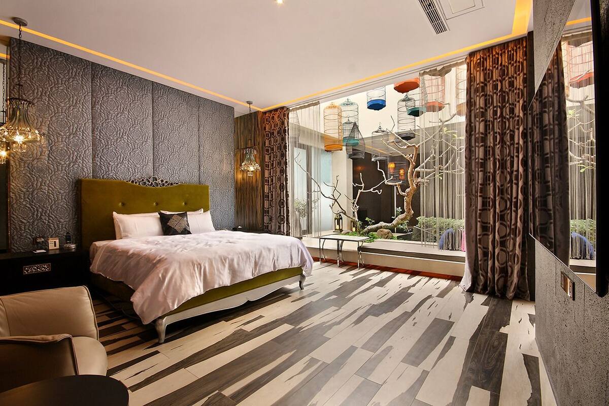 A modern bedroom with a large bed, a view of a courtyard, and a patterned wall.