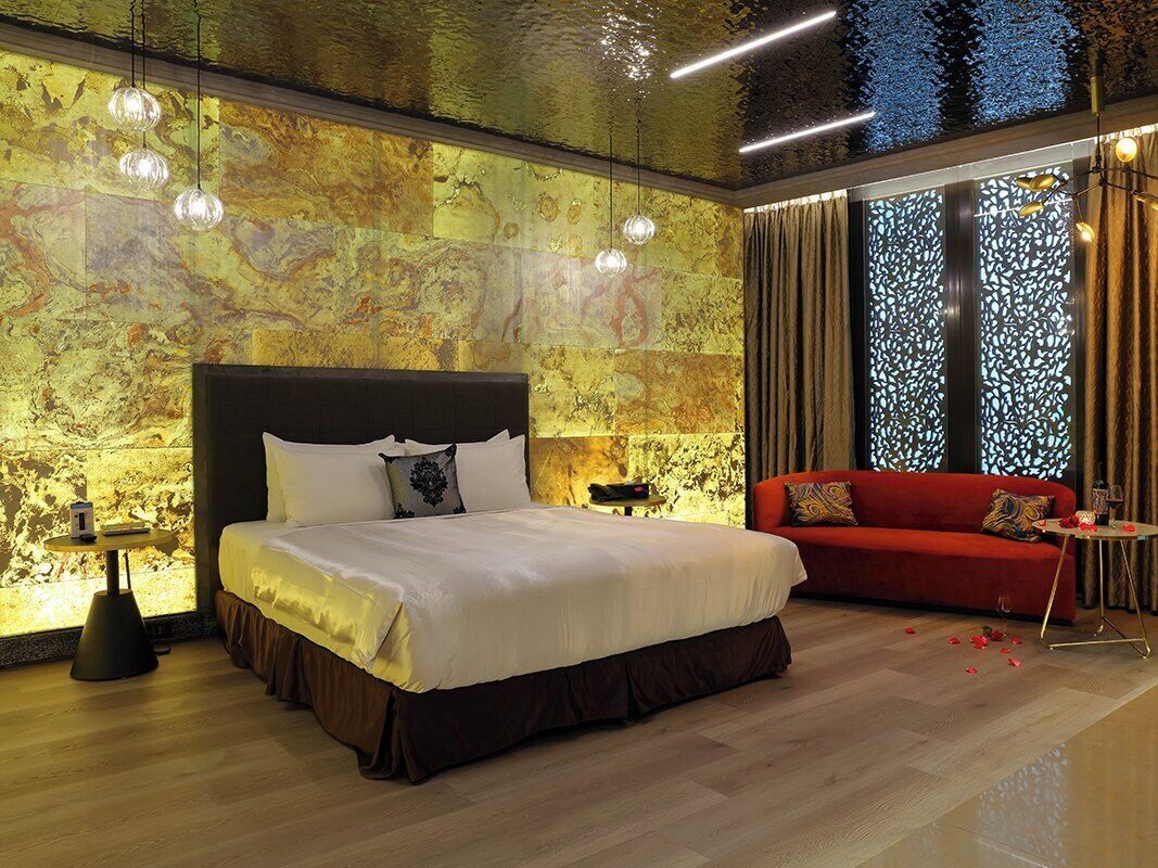 A modern hotel room with a large bed, a red sofa, and a decorative wall.
