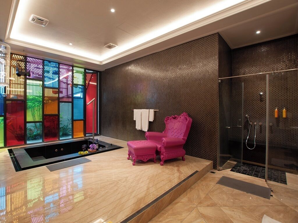 Un bany modern amb plat de dutxa de vidre, una cadira rosa i un element decoratiu de paret colorit.