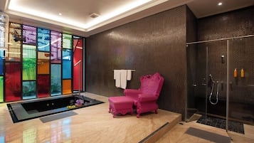 Un bany modern amb plat de dutxa de vidre, una cadira rosa i un element decoratiu de paret colorit.