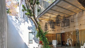 Un área de estar al aire libre moderna con techo de bambú, un árbol y una puerta de cristal que da al interior.