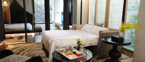 Una habitación de hotel con cama, sofá, mesa de comedor con comida y un jarrón con flores.