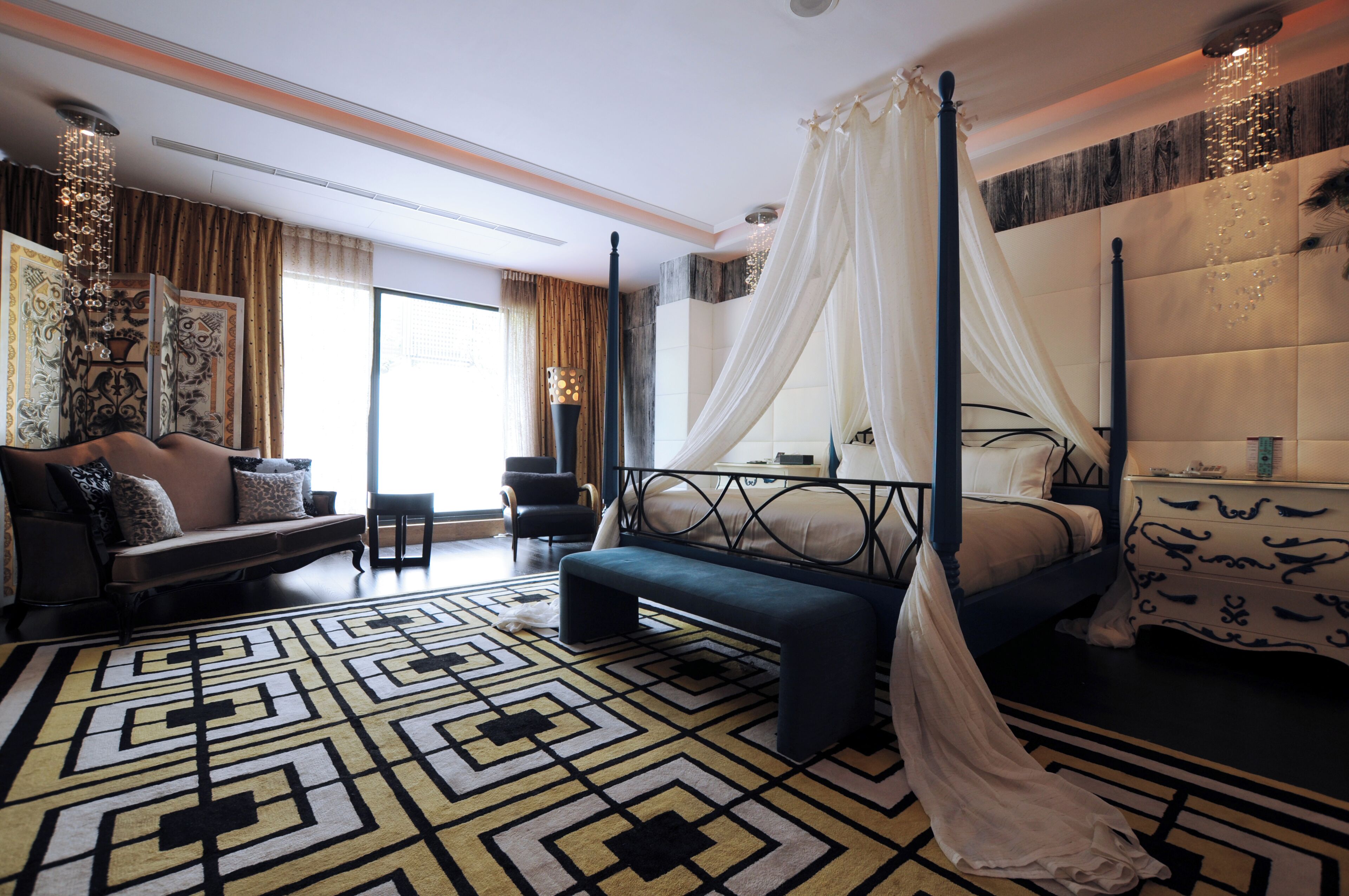 A modern bedroom with a four-poster bed, a sofa, and a patterned rug.