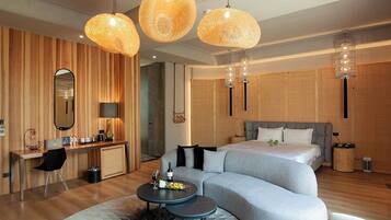 A modern hotel room with a large bed, a sofa, a desk, and a round table. There are three hanging lamps and a mirror on the wall.
