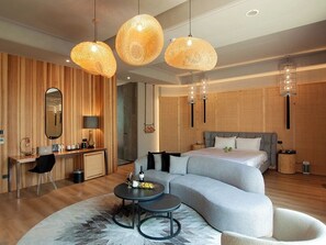 Habitación de hotel moderna con una cama grande, un sofá, un escritorio y una mesa redonda. Hay tres lámparas colgantes y un espejo en la pared.