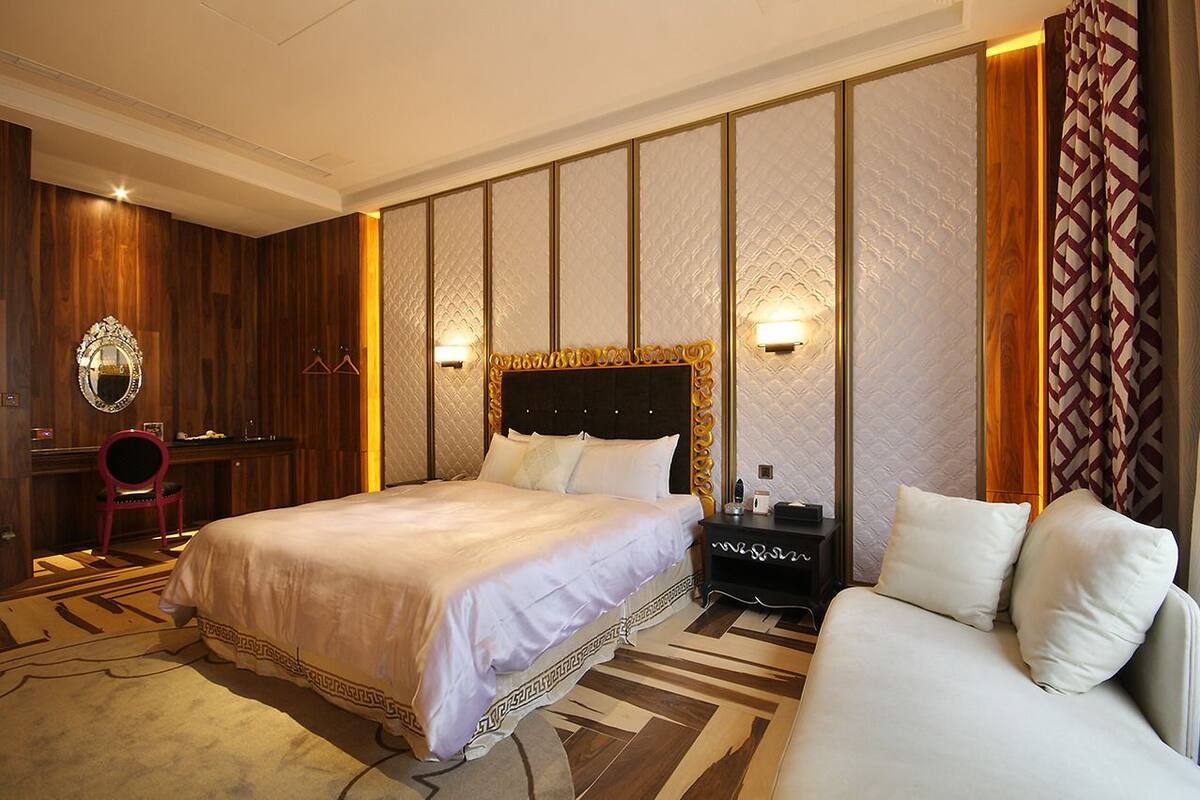 A hotel room with a large bed, a sofa, a desk, and a mirror.