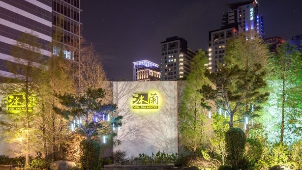Un hotel con un letrero grande, rodeado de árboles y edificios modernos al fondo.