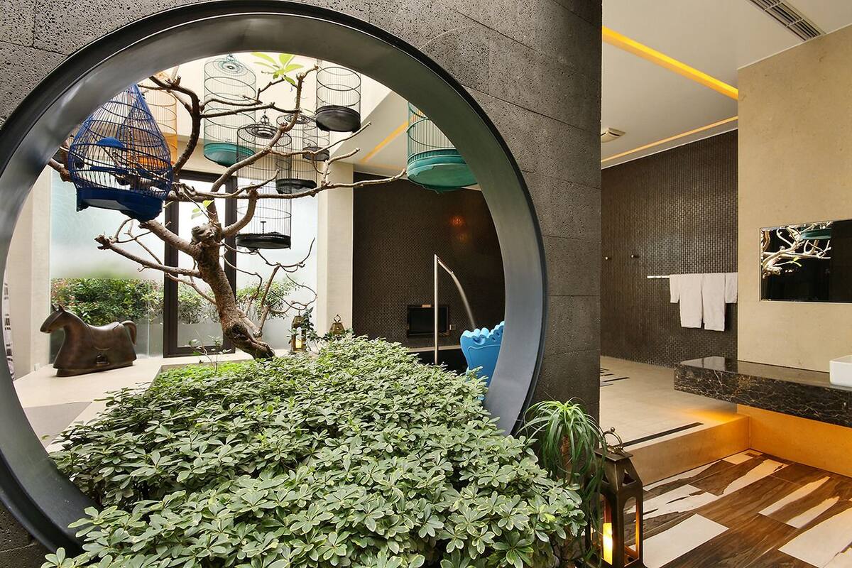A modern interior with a circular window, a tree sculpture, and a birdcage.
