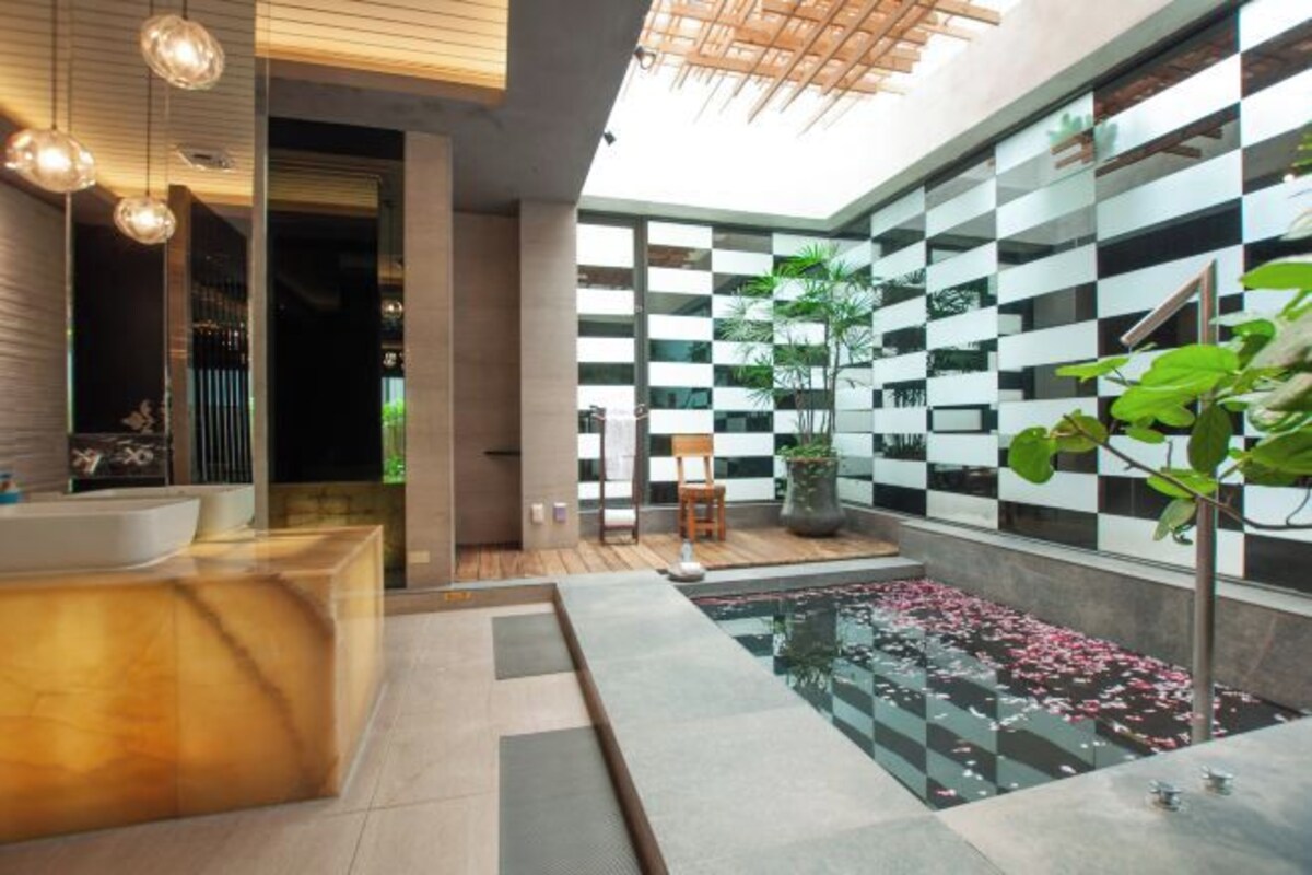 Un baño moderno con una bañera grande, un lavabo y un espejo. Hay una ventana pequeña y una planta.