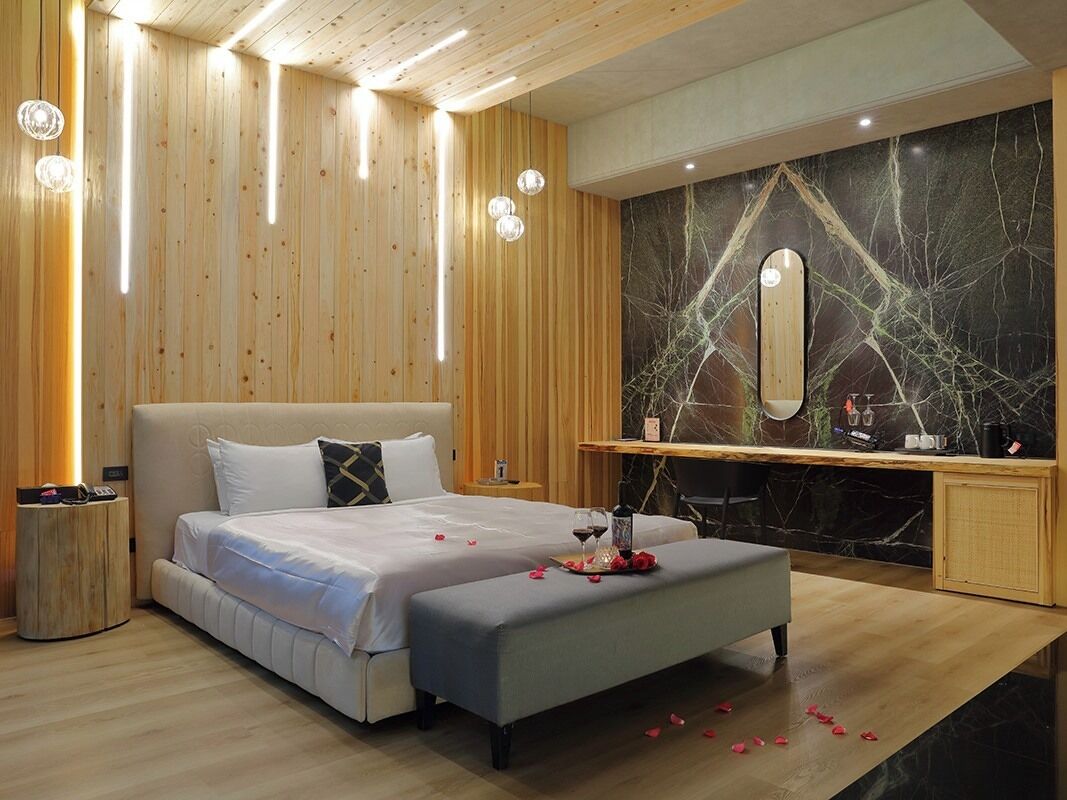 Een moderne slaapkamer met een groot bed, nachtkastjes, een kaptafel met spiegel en een houten plafond.
