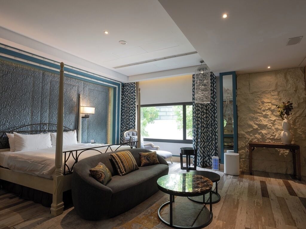 Een moderne hotelkamer met een hemelbed, een bank, een ronde salontafel en een accentmuur van steen.