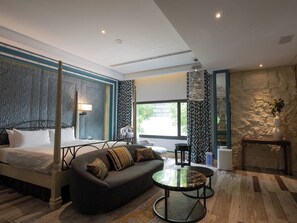Une chambre d’hôtel moderne avec un lit à baldaquin, un canapé, une table basse ronde et un mur décoratif en pierre.
