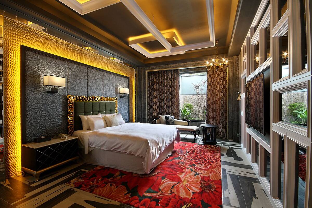 A spacious bedroom with a large bed, a nightstand, a desk, and a chair. There is a large window providing a view of the outdoors.
