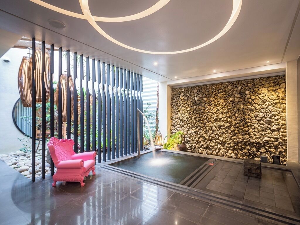 A modern interior with a stone wall, a pink chair, and a circular ceiling design.