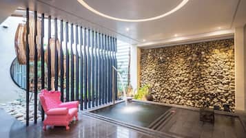 A modern interior with a stone wall, a pink chair, and a circular ceiling design.