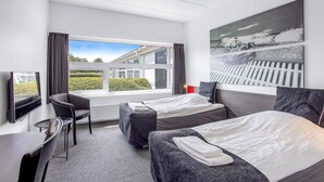 A hotel room with two beds, a desk, a chair, and a large window offering a view of the outside. - Sportshotel Vejen (Vejen)
