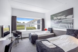 Habitación de hotel con dos camas, un escritorio, una silla y un ventanal con vistas al exterior.