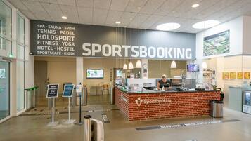 A sports booking counter with a sign listing amenities like spa, sauna, tennis, and fitness.