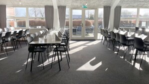 A conference room with tables and chairs, large windows, and an exit door. - Sportshotel Vejen (Vejen)
