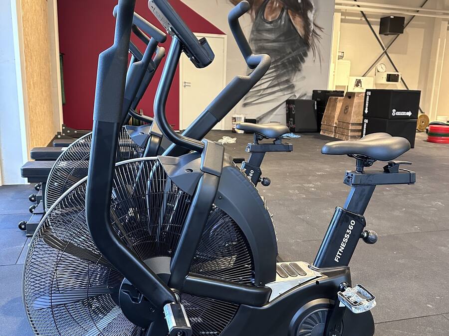 A stationary bike in a gym with a red wall and a large painting in the background.