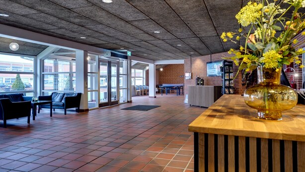 A spacious lobby with a tiled floor, seating area, and a reception desk with a vase of flowers. - Sportshotel Vejen (Vejen)