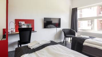 A hotel room with two beds, a desk with a computer and magazines, a TV, and a chair.