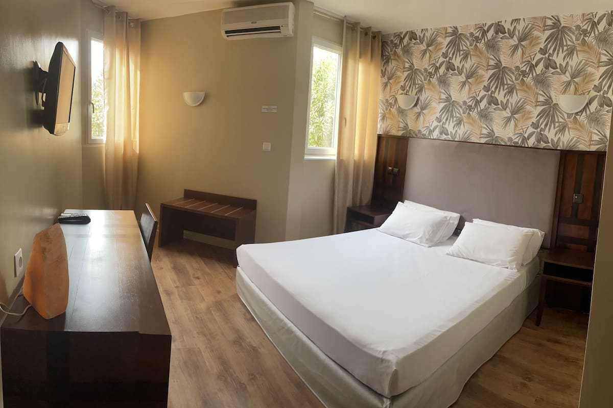 A hotel room with a bed, a desk, a chair, a small table, and a wall-mounted TV.