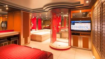 A modern hotel room with a large bed, a separate bathroom with a bathtub, and a television displaying 'CHABROL'.