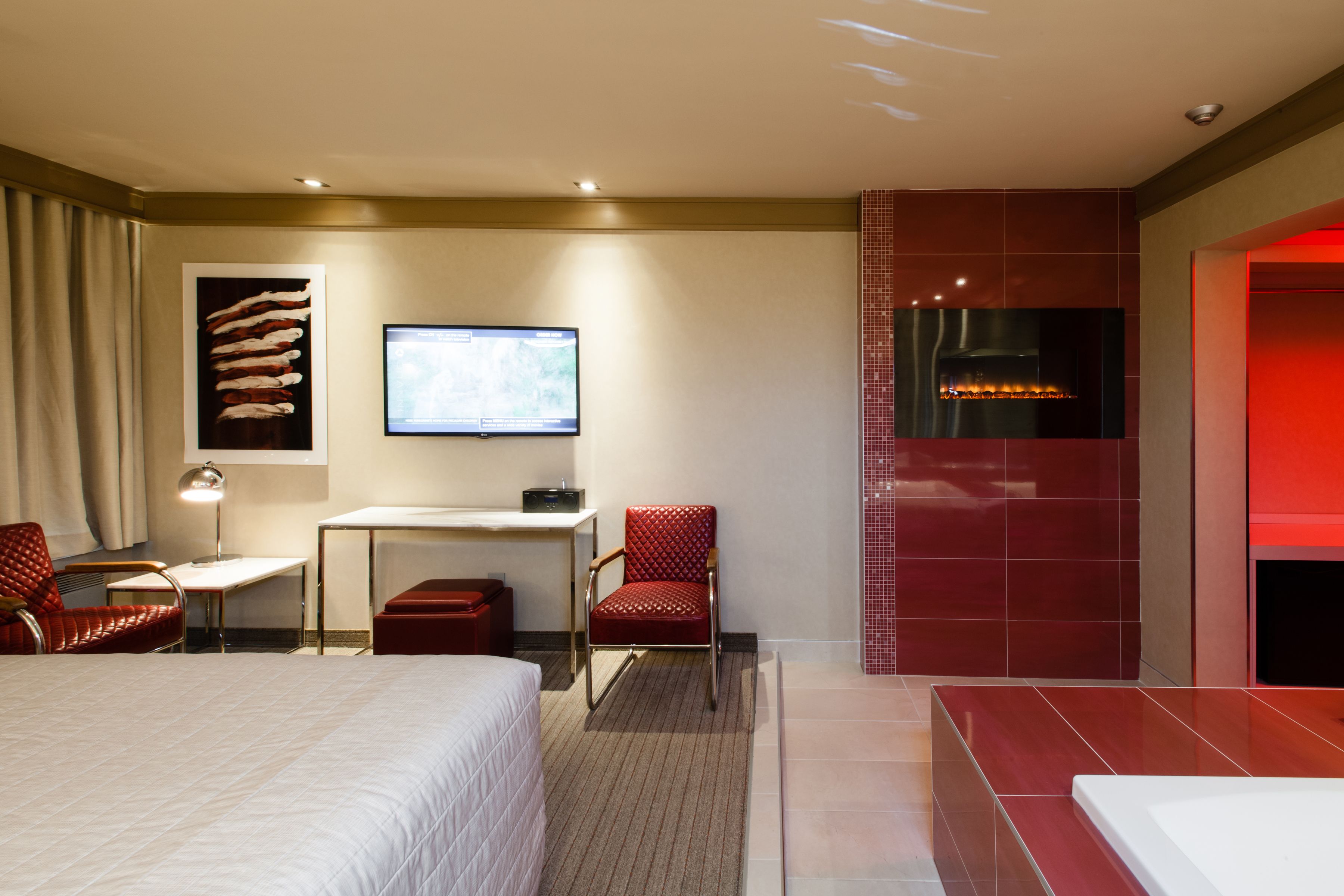Een hotelkamer met een bed, bureau, stoel, televisie en een open haard.
