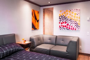 Une chambre d’hôtel moderne avec un canapé en cuir, une petite table sur laquelle se trouve un verre de jus d’orange, et deux œuvres d’art accrochées au mur.