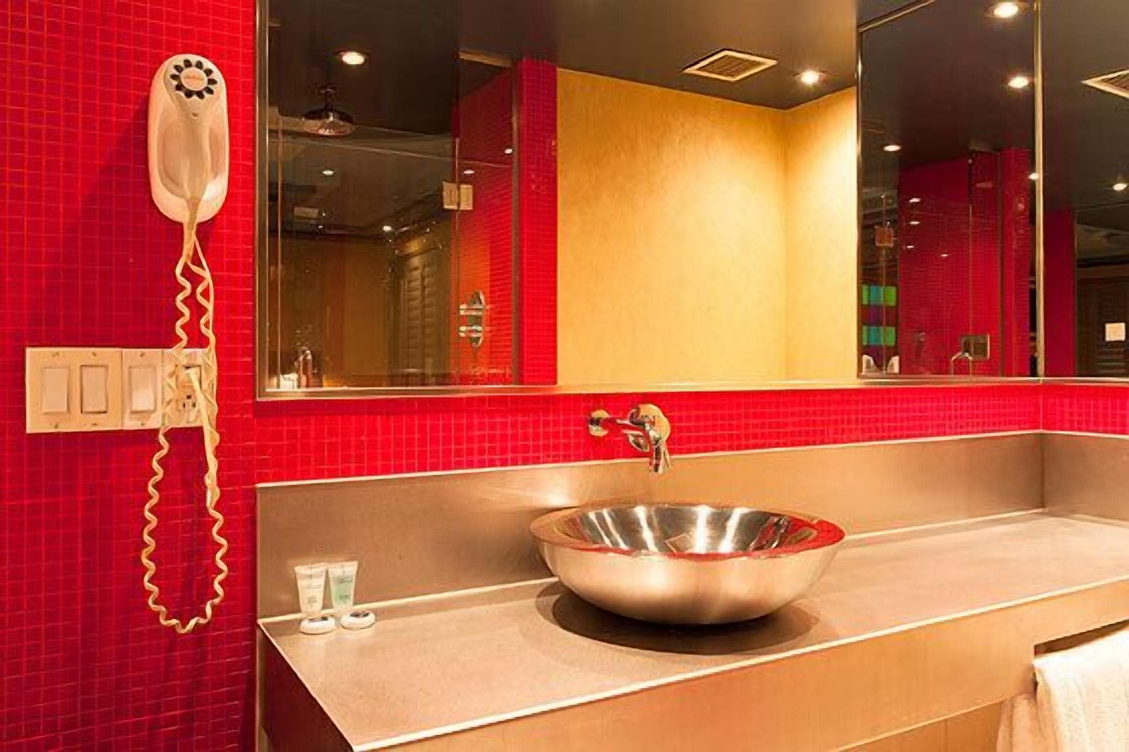 Ein Badezimmer mit roter Fliesenwand, einem Edelstahlwaschbecken und einem an der Wand montierten Föhn.