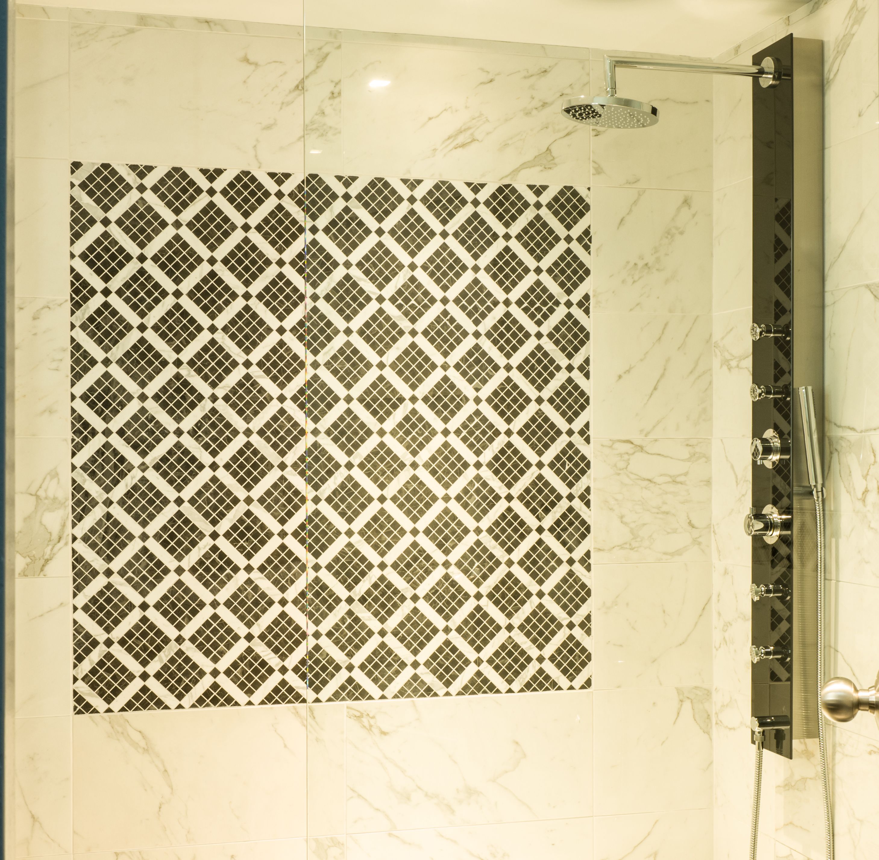 Une douche avec un mur recouvert de carreaux à motifs et une pomme de douche protégée par une paroi de verre.