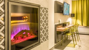 A hotel room with a bed featuring a red-lit headboard, a desk with a chair, and a television mounted on the wall. - Le Chabrol Hotel & Suites (Montreal)
