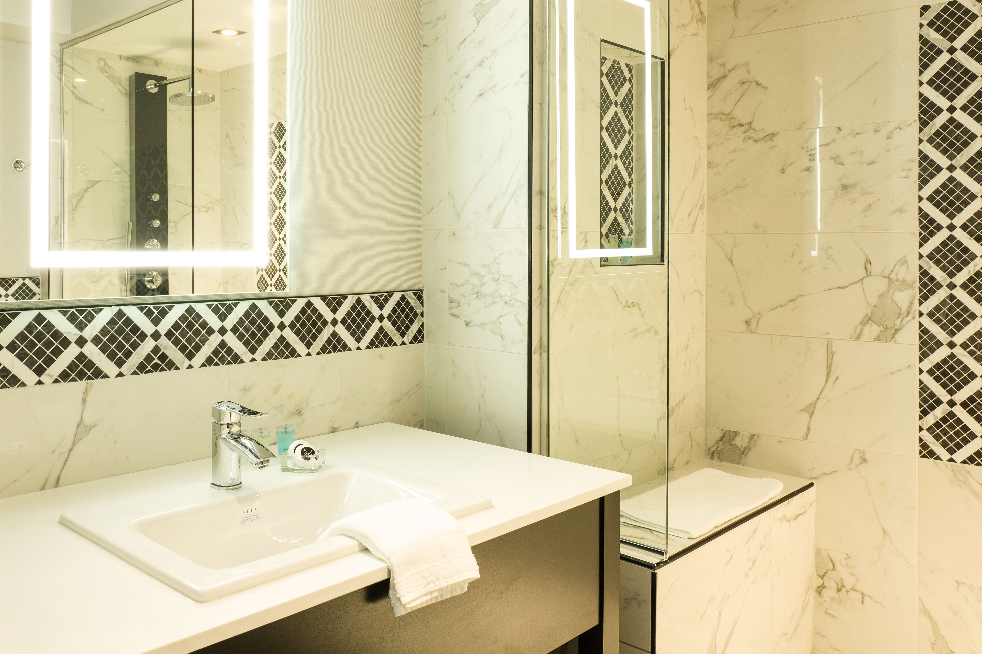A modern bathroom with a marble sink, a large mirror, and a glass shower enclosure.