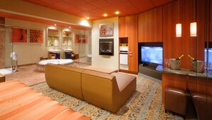 A hotel room with a large bed, a sofa, a TV, a minibar, and a bathroom with a glass shower. - Le Chabrol Hotel & Suites (Montreal)