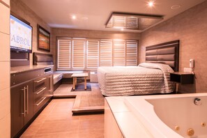 Una habitación de hotel moderna con una cama grande, un área de estar separada, una bañera y un televisor en la pared.