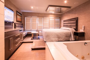 Une chambre d’hôtel moderne dotée d’un grand lit, d’un coin salon séparé, d’une baignoire et d’un téléviseur fixé au mur.