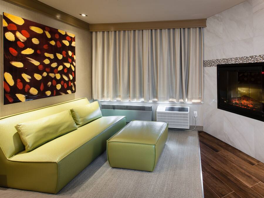 A modern living room with a green sofa, a small ottoman, a fireplace, and a large abstract painting on the wall.